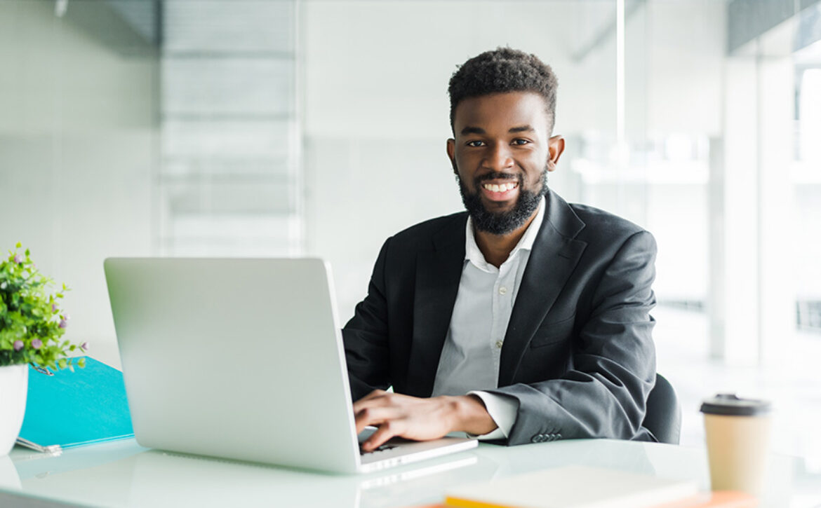 Portrait of handsome African black young business man working on laptop at office desk