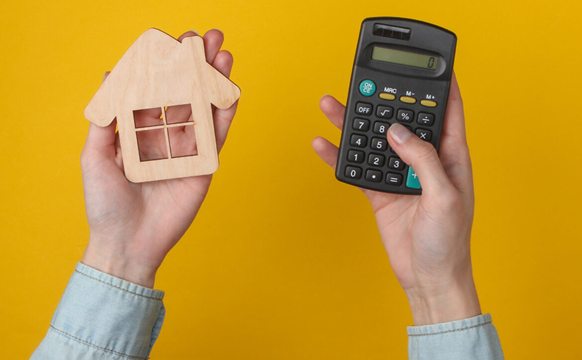 Calculation of the cost of housing, rent. Female hand uses calculator and hold house figure on yellow background. Top view