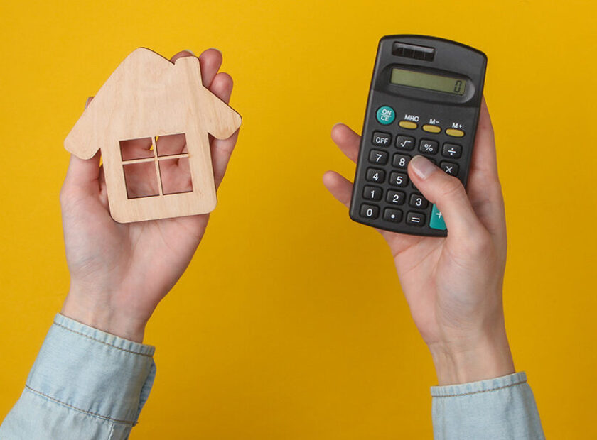 Calculation of the cost of housing, rent. Female hand uses calculator and hold house figure on yellow background. Top view