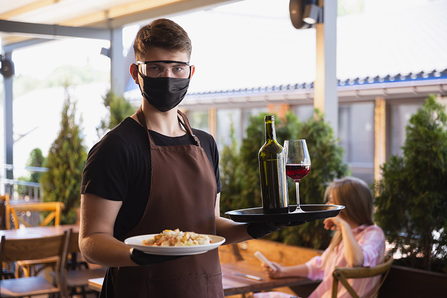 The waiter works in a restaurant in a medical mask, gloves during coronavirus pandemic