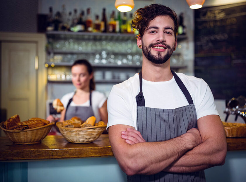 Smiling waiter standing with arms crossed in cafÃ©