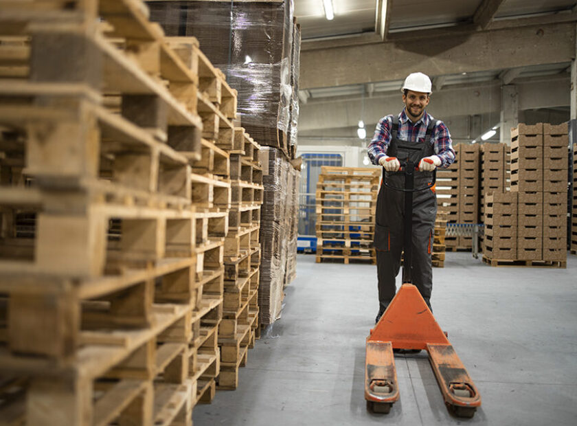 Skilled warehouse employee pushing manual pallet jack and workin