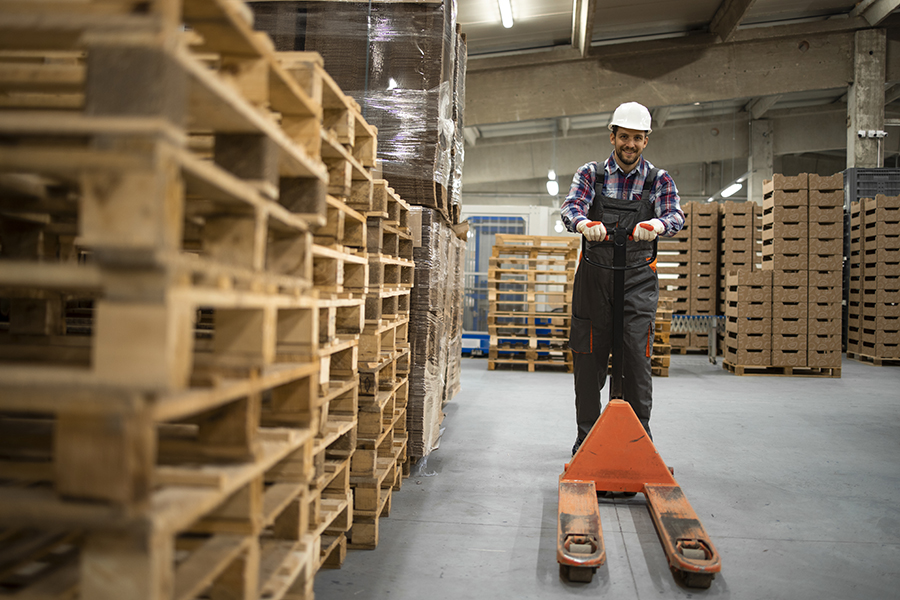 Skilled warehouse employee pushing manual pallet jack and workin
