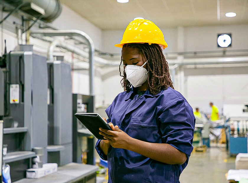 African American female factory worker in mask holding tablet
