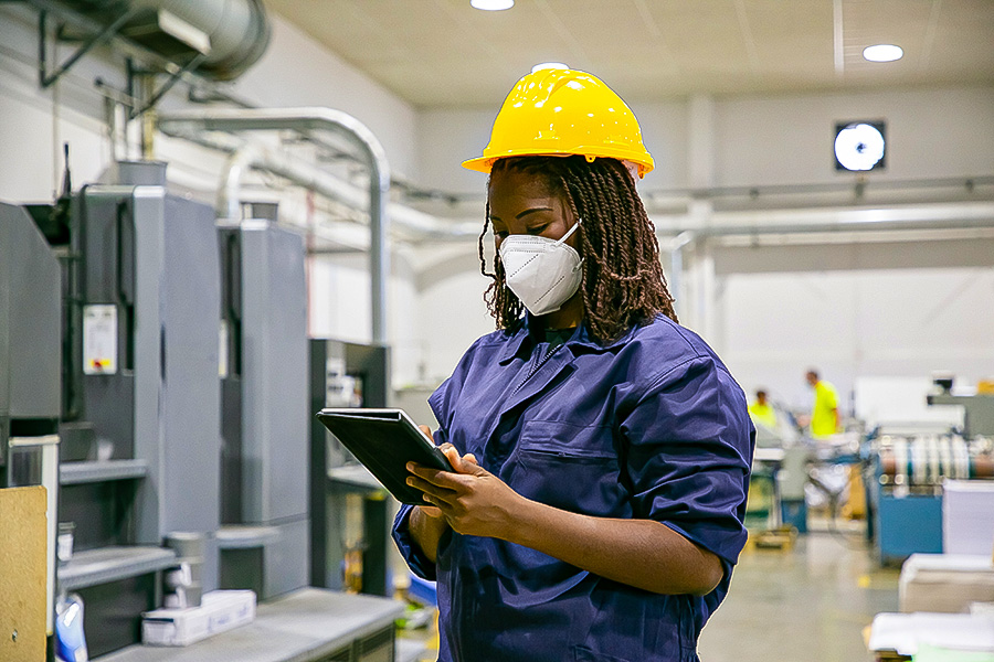 African American female factory worker in mask holding tablet