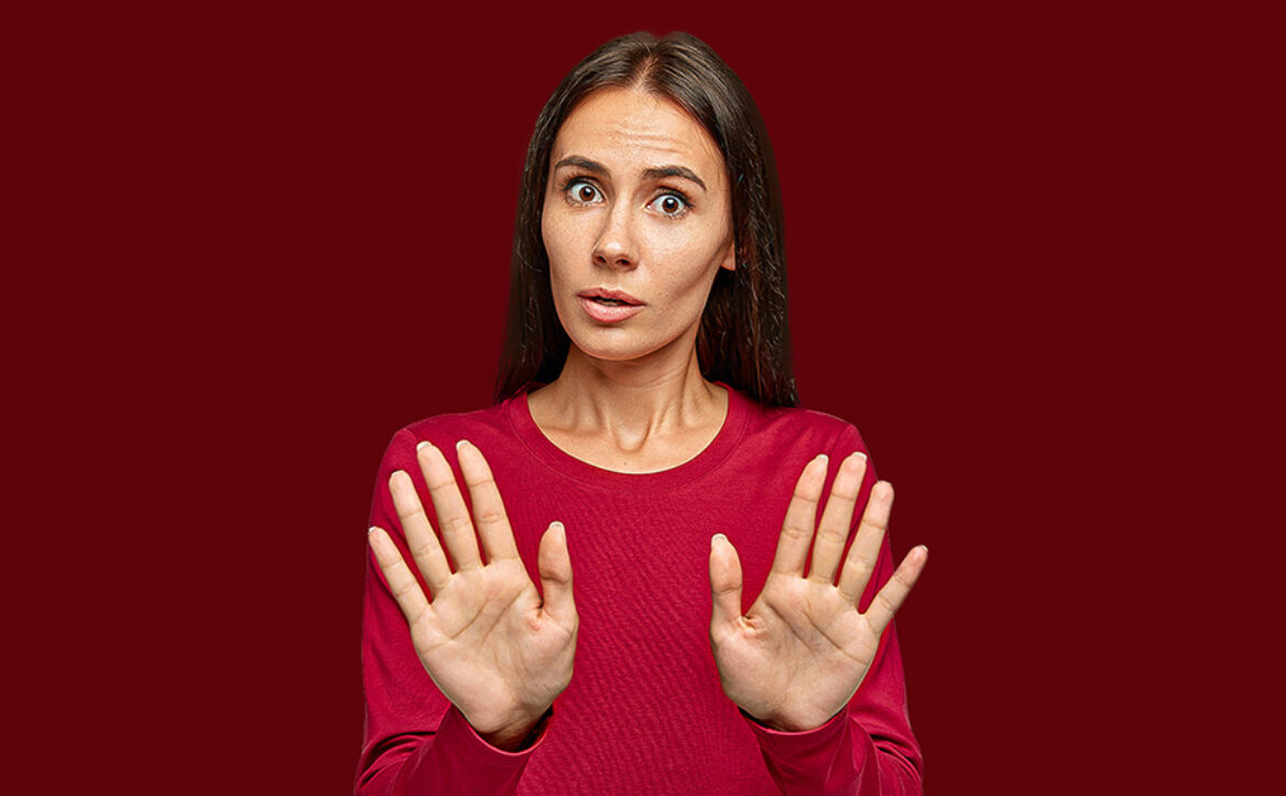 Oh no, stop there. Serious beautiful woman rejects offer, pulls palms in no gesture, asks to stop this, wears red clothes, stands against white background, tries protect herself from wrong doing
