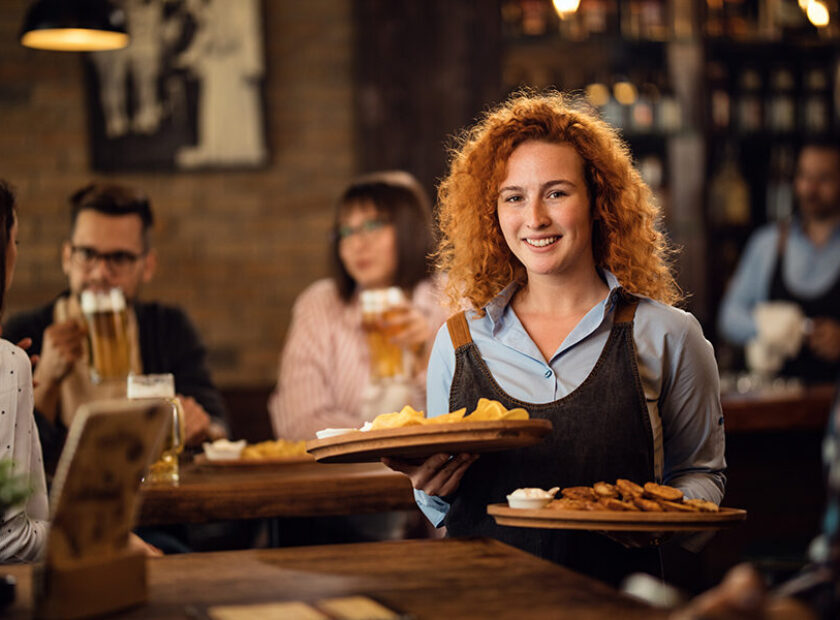 Young happy waitress serving her guest in a pub.