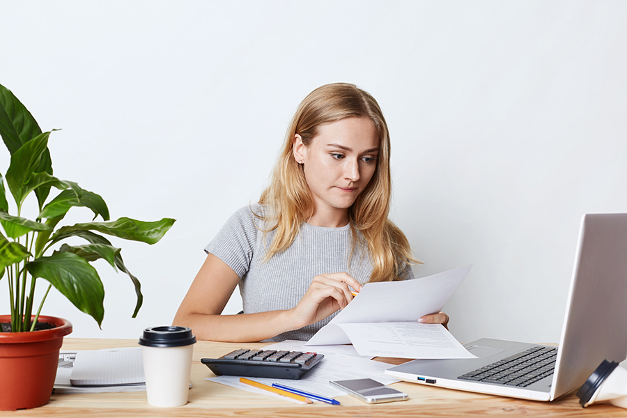 Portrait of young businesswoman working with laptop and calculator, looking attentively at documents, calcualting bills of company, making financial report. People, career and business concept